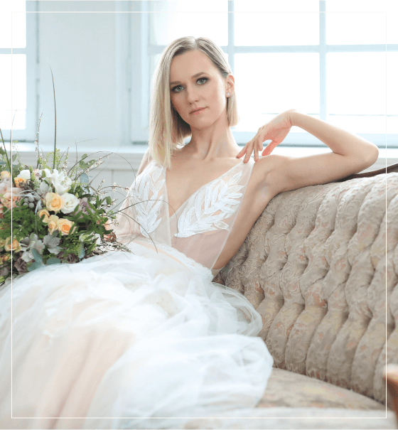 Bride in a lace gown holding a bouquet by a window